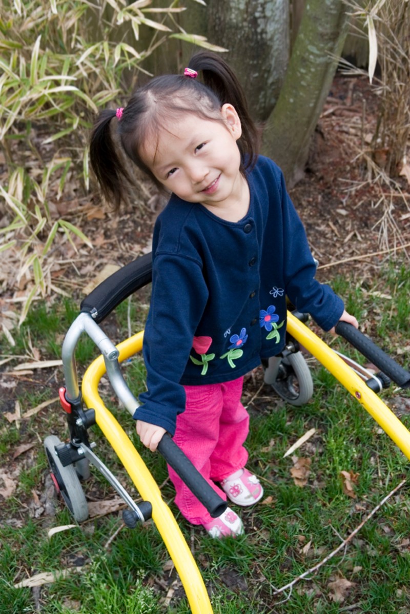 Niña pequeña sonriente sostiene con sus manos las barras de una estructura móvil para caminar