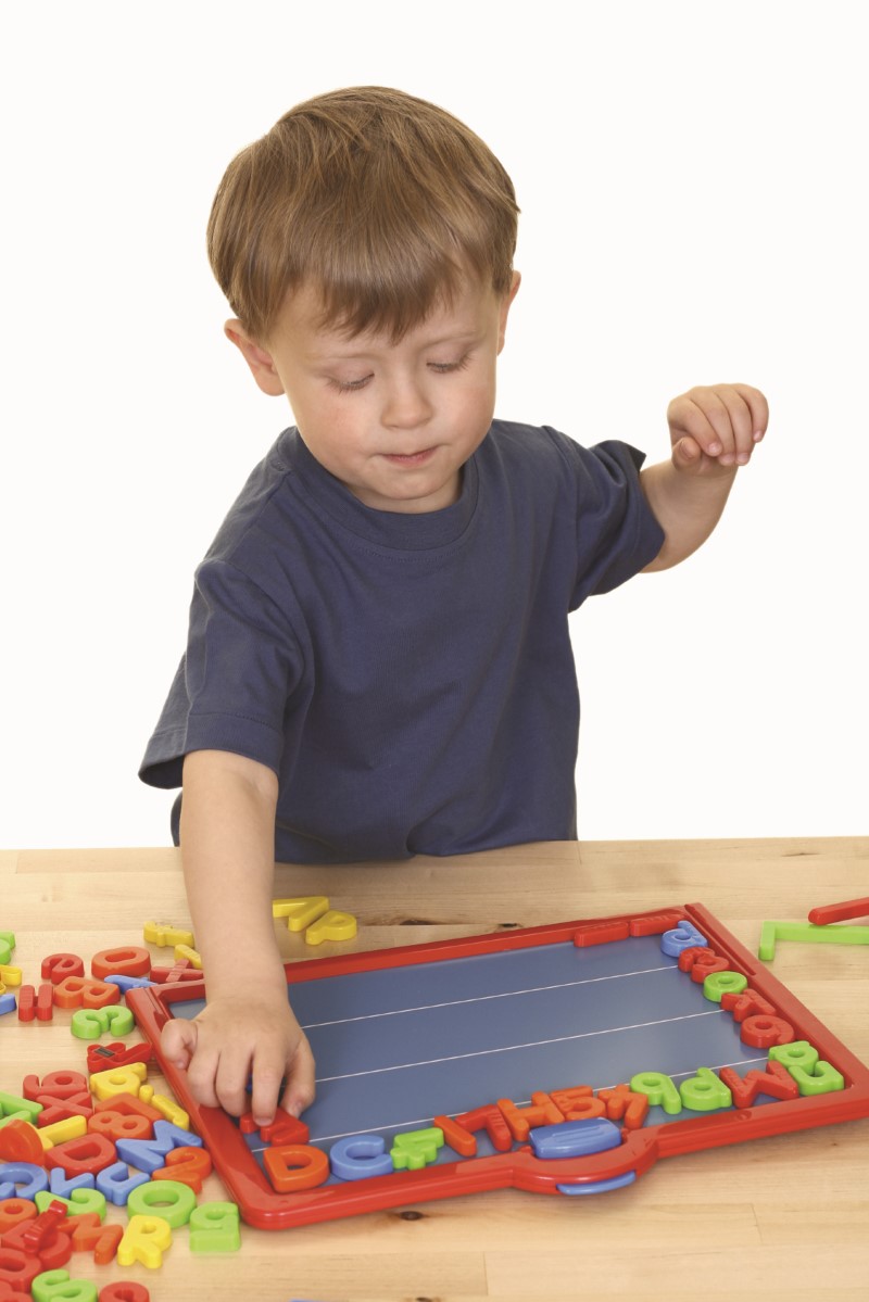 Niño pequeño observa atentamente y coloca con una mano letras y números sobre una pizarra magnética