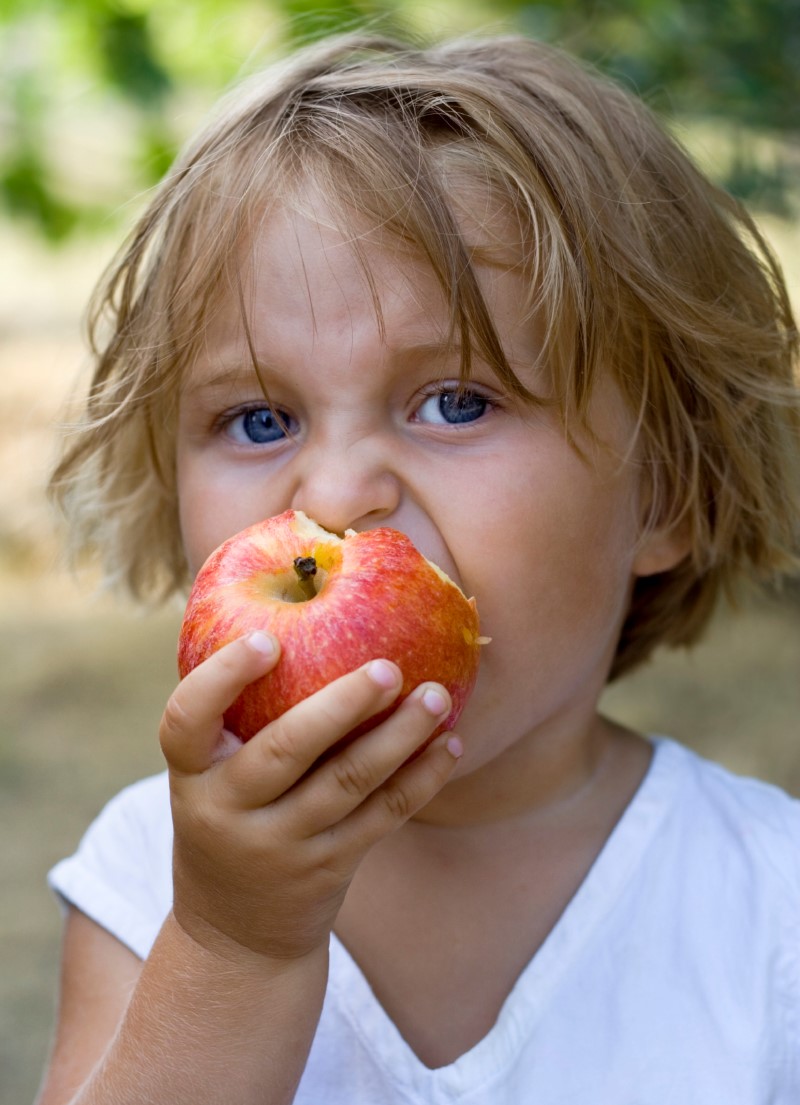 Niña pequeña dándole un mordisco a una manzana roja que sostiene en su mano