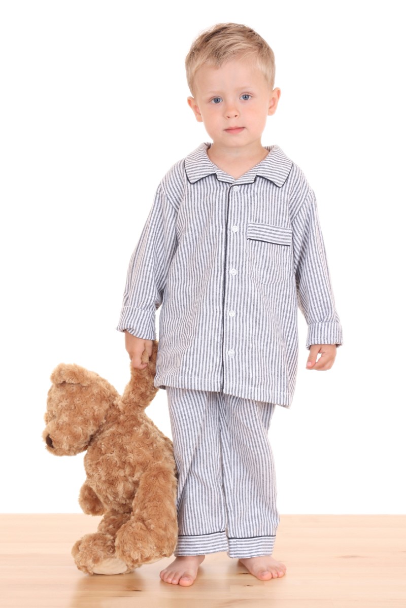 Niño pequeño en sus pijamas/piyamas de pie mientras sosotiene un muñeco de peluche en su mano