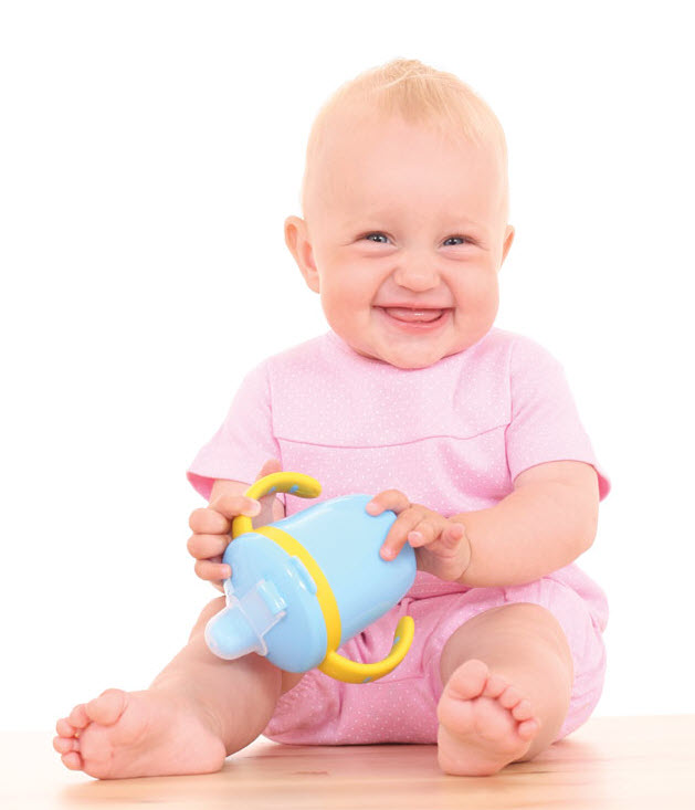 Bebé sonriente, sentada(o), vestido(a) de traje de verano rosa sostiene su tacita de beber (sippy) con ambas manos