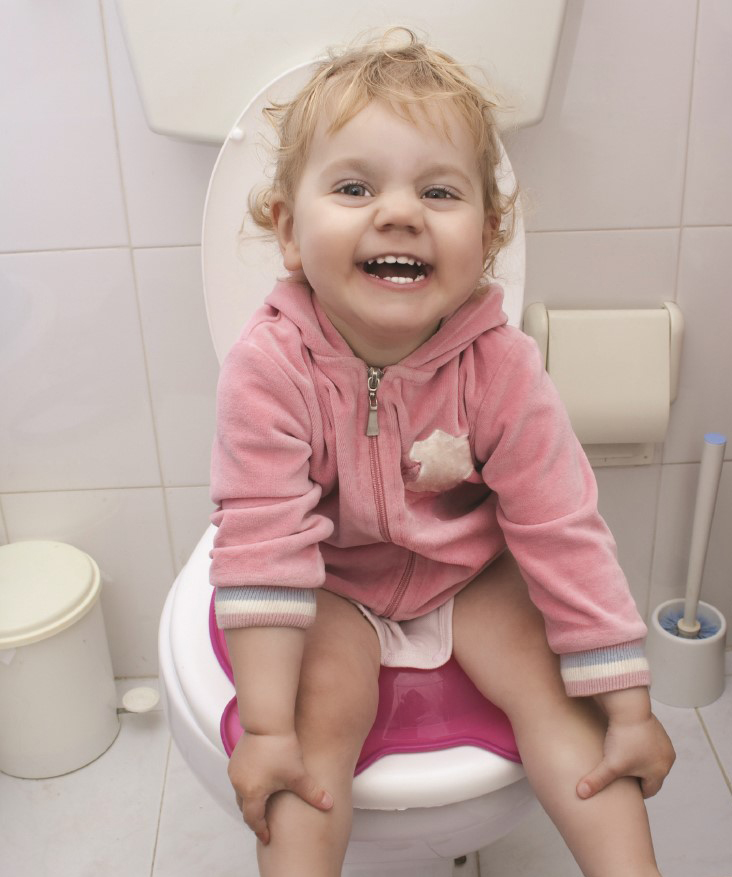 Niña pequeña sonríe sentada en una bacinilla de plástico posada sobre la poceta