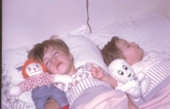Dos niños pequeños duermen juntos en sus camas con peluches a sus lados