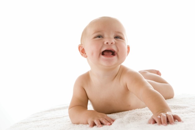 Bebé sonriente sobre una manta, boca abajo, con su cabeza y tronco erguidos, los brazos y manos sosteniéndole