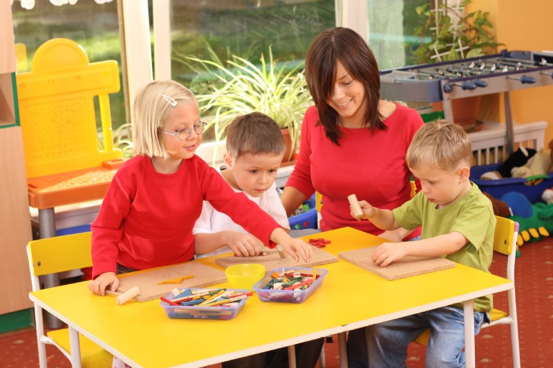 Educadora juega con tres niños/niñas utilizando piezas de madera de colores sobre tableros en una guardería/jardín de infancia